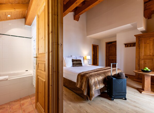 A bedroom with a bed, a suitcase, a wooden cabinet, and a bathroom with a bathtub. - Hôtel Saint Martin (Les Belleville)