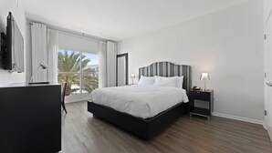 A modern hotel room with a large bed, a desk, a chair, and a window with curtains.