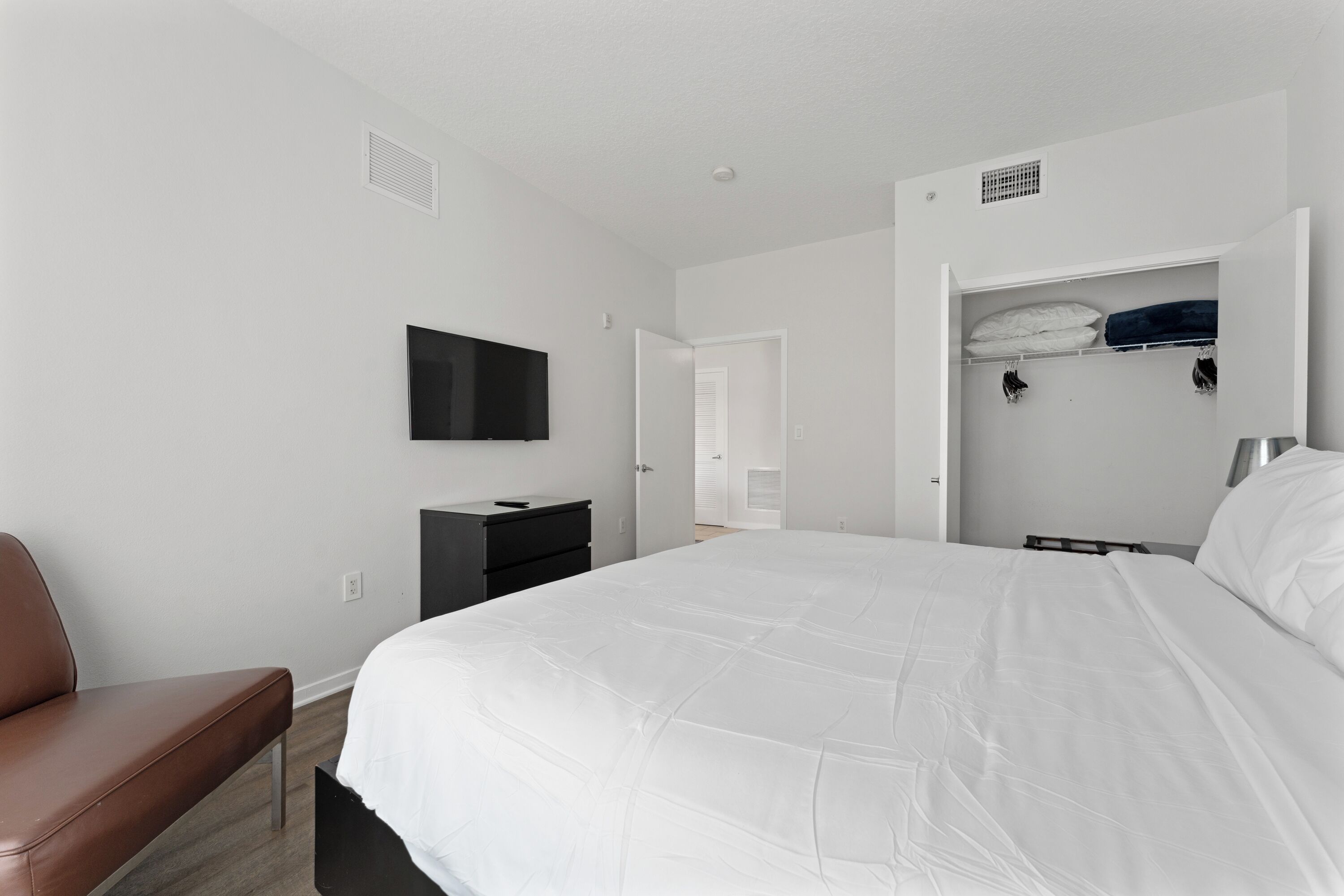 Une chambre avec un grand lit, un téléviseur fixé au mur, une armoire et un banc.