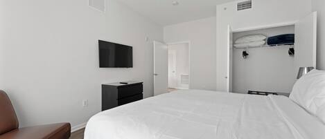 Une chambre avec un grand lit, un téléviseur fixé au mur, une armoire et un banc.