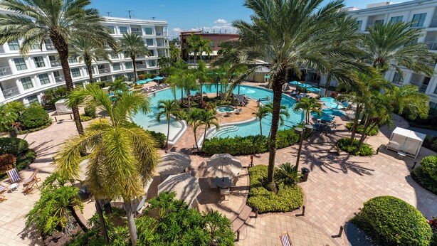 A resort with a central swimming pool surrounded by palm trees and sun loungers.