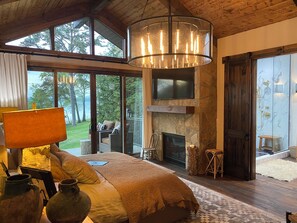 A spacious bedroom with a large bed, a fireplace, a television, and a view of the outdoors.
