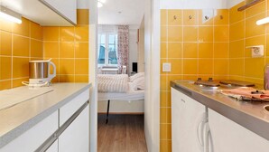 A compact kitchen with a bed in the background, a kettle, and a stove. - Apartment 'Anker' with Shared Terrace and Wi-Fi (Cuxhaven)