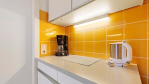 A kitchen with a coffee maker and a kettle on the counter, a white cabinet below, and orange tiles on the wall. - Apartment 'Anker' with Shared Terrace and Wi-Fi (Cuxhaven)
