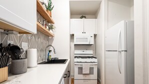 Una cocina moderna con armarios blancos, un refrigerador de acero inoxidable, un microondas y una estufa a gas.