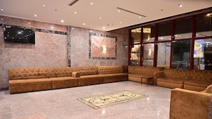 Een ruime lobby met een grote hoekbank, een getextureerd vloerkleed en een groot raam met uitzicht.