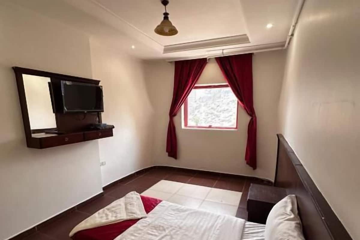 Une chambre à coucher avec un lit, un téléviseur fixé au mur et une fenêtre avec des rideaux.