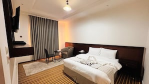 Hotelkamer met een bed, bureau, stoel, televisie en raam met gordijnen.