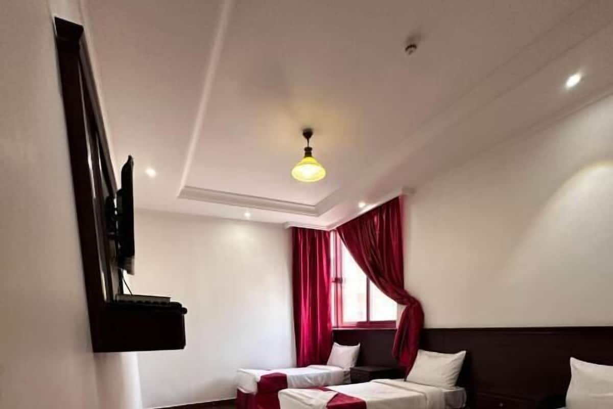 Une chambre d’hôtel avec trois lits, chacun doté de draps rouges et blancs, un téléviseur à écran plat fixé au mur et un luminaire au plafond.