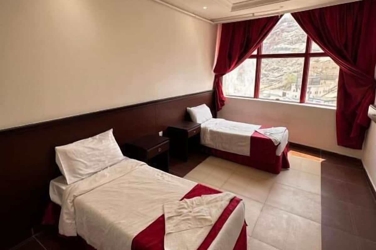 Une chambre d’hôtel avec deux lits, une grande fenêtre avec des rideaux, un luminaire au plafond et une vue sur l’extérieur.