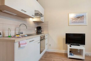 A kitchen with a built-in oven, a coffee maker, a sink, and a TV on a stand.