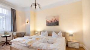 Un letto rifatto con copriletto floreale, un comodino con lampada, una sedia e un quadro appeso al muro.