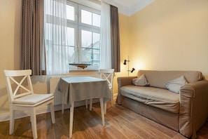 A room with a white table, a beige sofa, a window with curtains, and a small sailboat model.