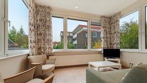 A sunroom with a TV, seating, and a view of buildings.