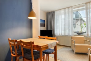 Angolo ristoro con tavolo e sedie, televisione e vista su una casa dalla finestra.