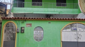 A two-story building with a green facade, a balcony with white railings, and barred garage doors. - Cozy place in Perdeira (Belém)