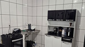 A compact kitchen with white tiled walls, a black stove, a coffee maker, and a dishwasher. - Cozy place in Perdeira (Belém)
