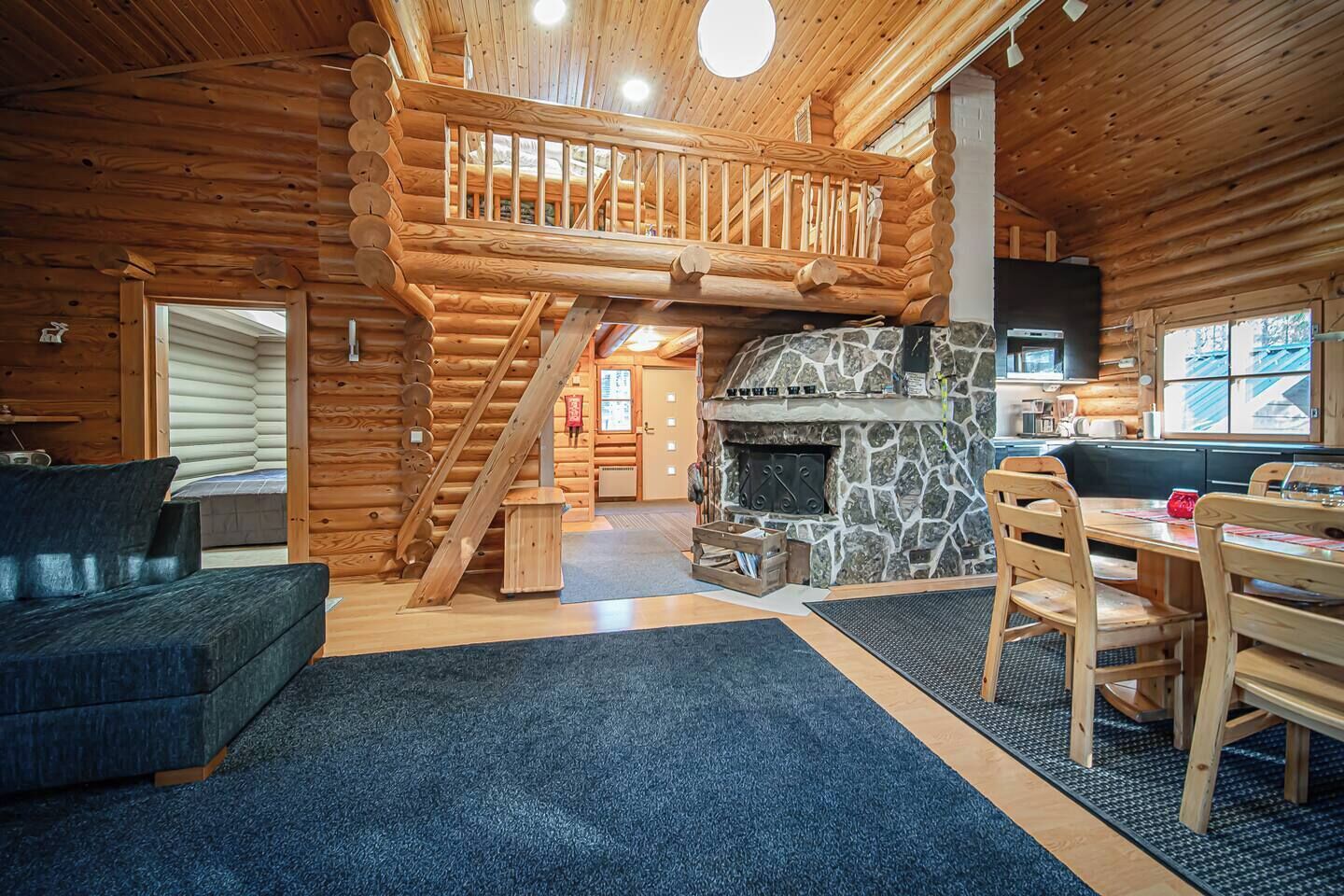 L’intérieur d’une cabane en rondins, avec une cheminée en pierre, un escalier en bois et un coin repas.