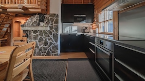Interior de una cabaña de troncos con chimenea de piedra, electrodomésticos de cocina modernos y comedor con mobiliario de madera.
