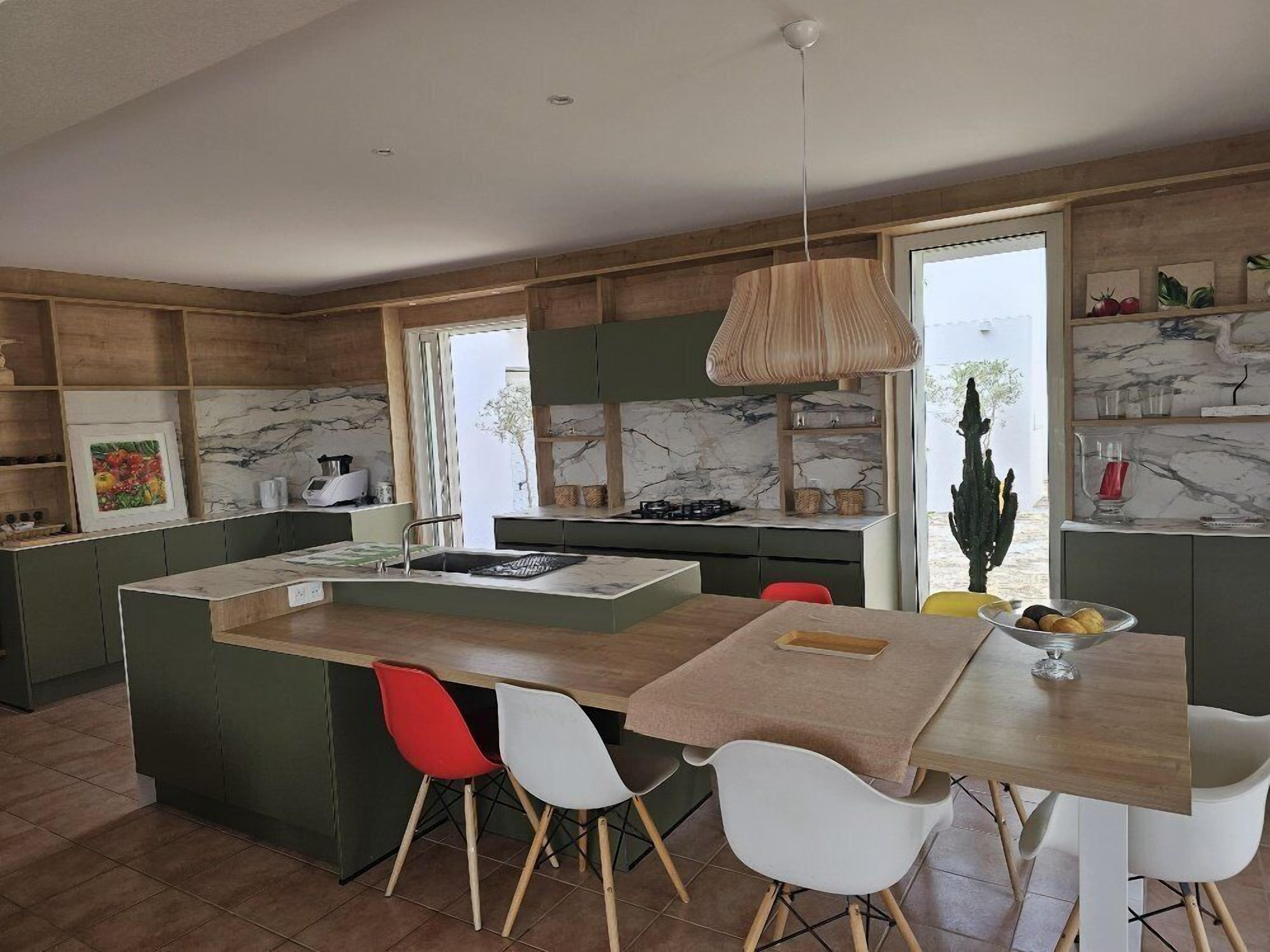 A modern kitchen with a central island, red and white chairs, and a hanging light fixture.