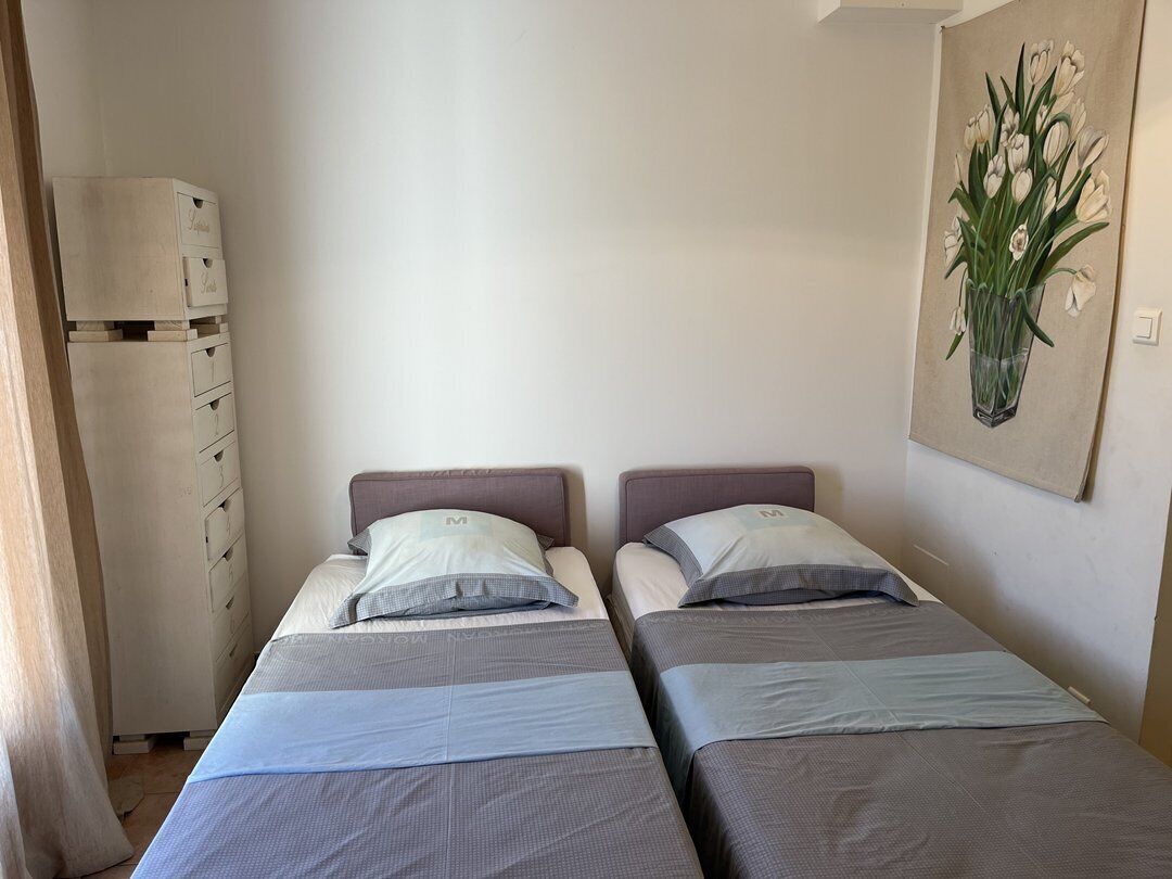 A room with two beds, a dresser, and a painting of flowers on the wall.