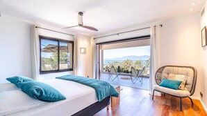Ein Schlafzimmer mit einem großen Bett, einem Sessel und Blick ins Freie.