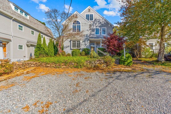 A two-story house with a stone wall and a gravel driveway.