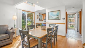 A dining area with a wooden table and chairs, a sofa, and a view through large windows.
