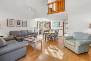 A spacious living room with a grey sofa, a light blue armchair, and a wooden dining table.