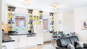A modern kitchen with white cabinets, a black countertop, and a dining area with a black leather sofa. - Apartment 'Ferienwohnung' with Balcony and Wi-Fi (Horumersiel-Schillig)