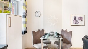 A dining area with a table set for two, a clock on the wall, and a framed picture. - Apartment 'Ferienwohnung' with Balcony and Wi-Fi (Horumersiel-Schillig)