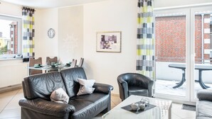 A modern living room with a leather sofa, a coffee table, and a dining area with chairs and a table. - Apartment 'Ferienwohnung' with Balcony and Wi-Fi (Horumersiel-Schillig)