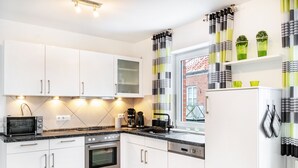 A modern kitchen with white cabinets, a built-in oven, a microwave, and a coffee maker. - Apartment 'Ferienwohnung' with Balcony and Wi-Fi (Horumersiel-Schillig)
