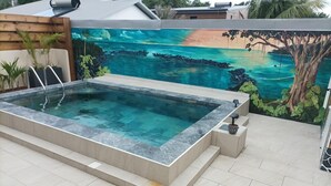 Banyera hidromassatge rectangular amb un emmarcament de pedra, amb un mural al fons que representa una platja tropical.