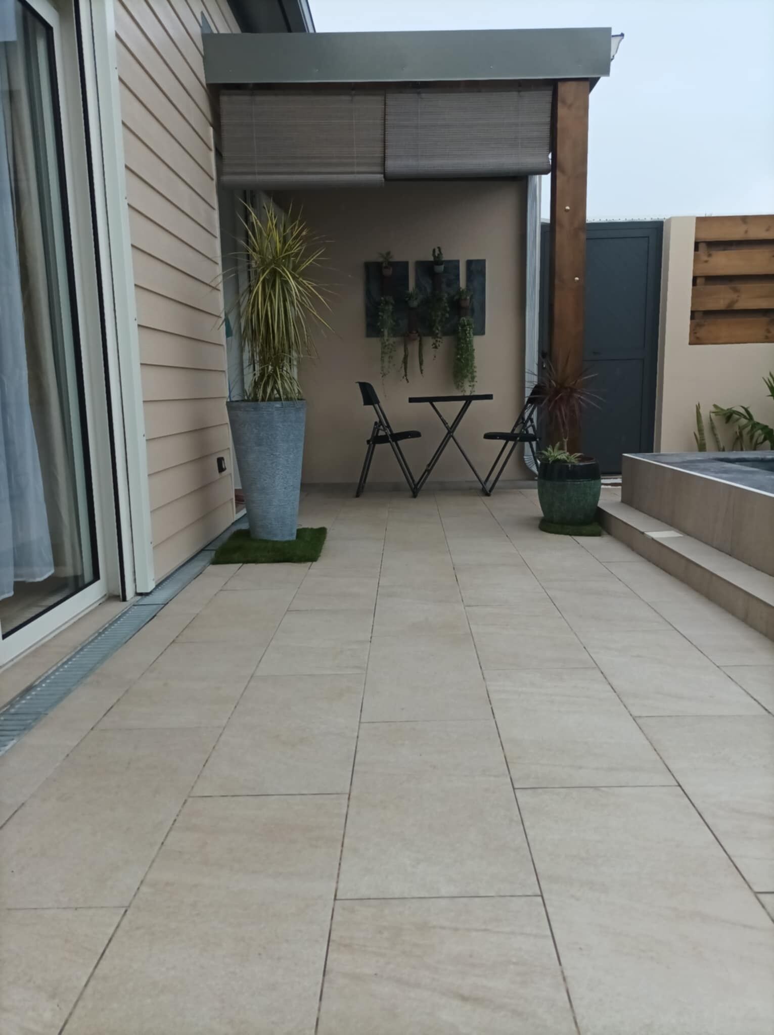 A modern patio area with a tiled floor, two black folding chairs, a small table, and potted plants.