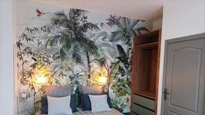 Un dormitori amb un llit, dues làmpades de nit, un armari i un mural amb temàtica tropical a la paret.