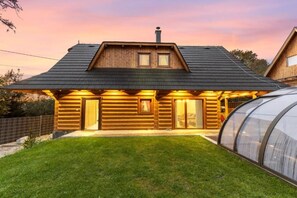 Eine Blockhütte mit geneigtem Dach, ein großes Glashaus, das seitlich angebaut ist, und ein gepflegter Rasen.