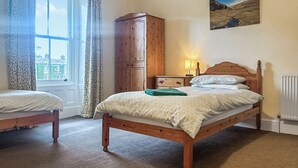 A bedroom with two single beds, a wooden wardrobe, a nightstand with a lamp, and a painting on the wall.