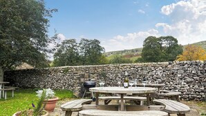 A stone wall, wooden picnic table, and a bottle of wine.