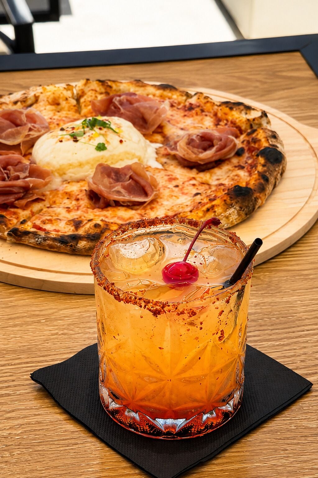 A pizza with prosciutto and a creamy topping on a wooden board.