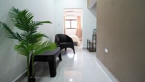 A narrow hallway with a black wicker chair, a small table with a potted plant, and a bed in the background. - La Palma Experience (Panama City)