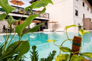 An indoor swimming pool with a view of a building with balconies and outdoor seating.