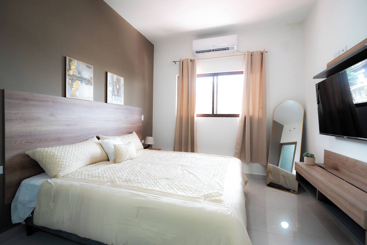 A modern bedroom with a large bed, a TV, and a mirror.