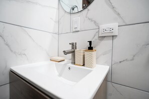 A bathroom with a white sink, a mirror, a soap dispenser, and a power outlet on the wall. - La Palma Experience (Panama City)