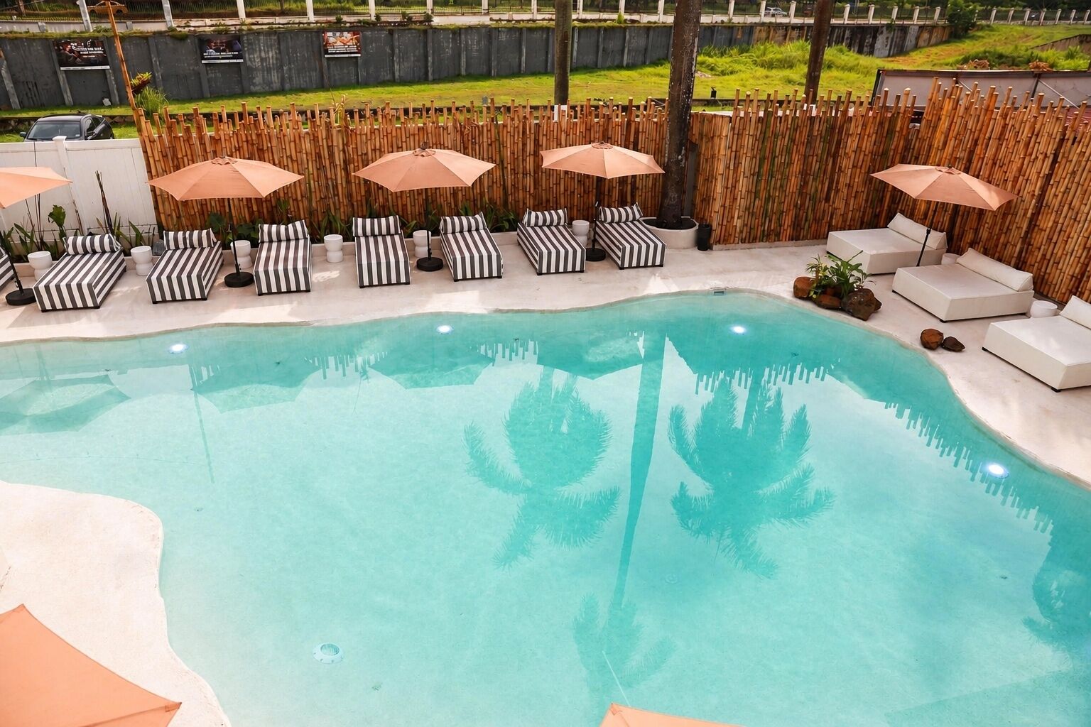 A swimming pool with lounge chairs and umbrellas, surrounded by a bamboo fence.