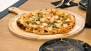 A pizza on a wooden board on a table with a black plate and cutlery beside it. - La Palma Experience (Panama City)