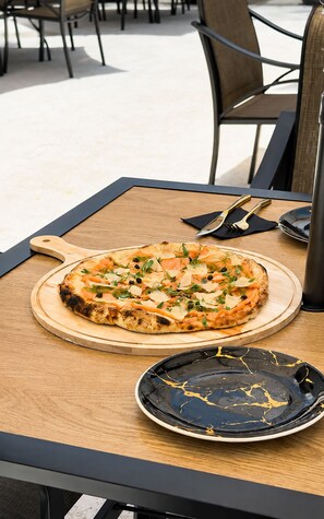 Eine Pizza auf einem Holzboden auf einem Tisch, nebenan ein schwarzer Teller und Besteck.