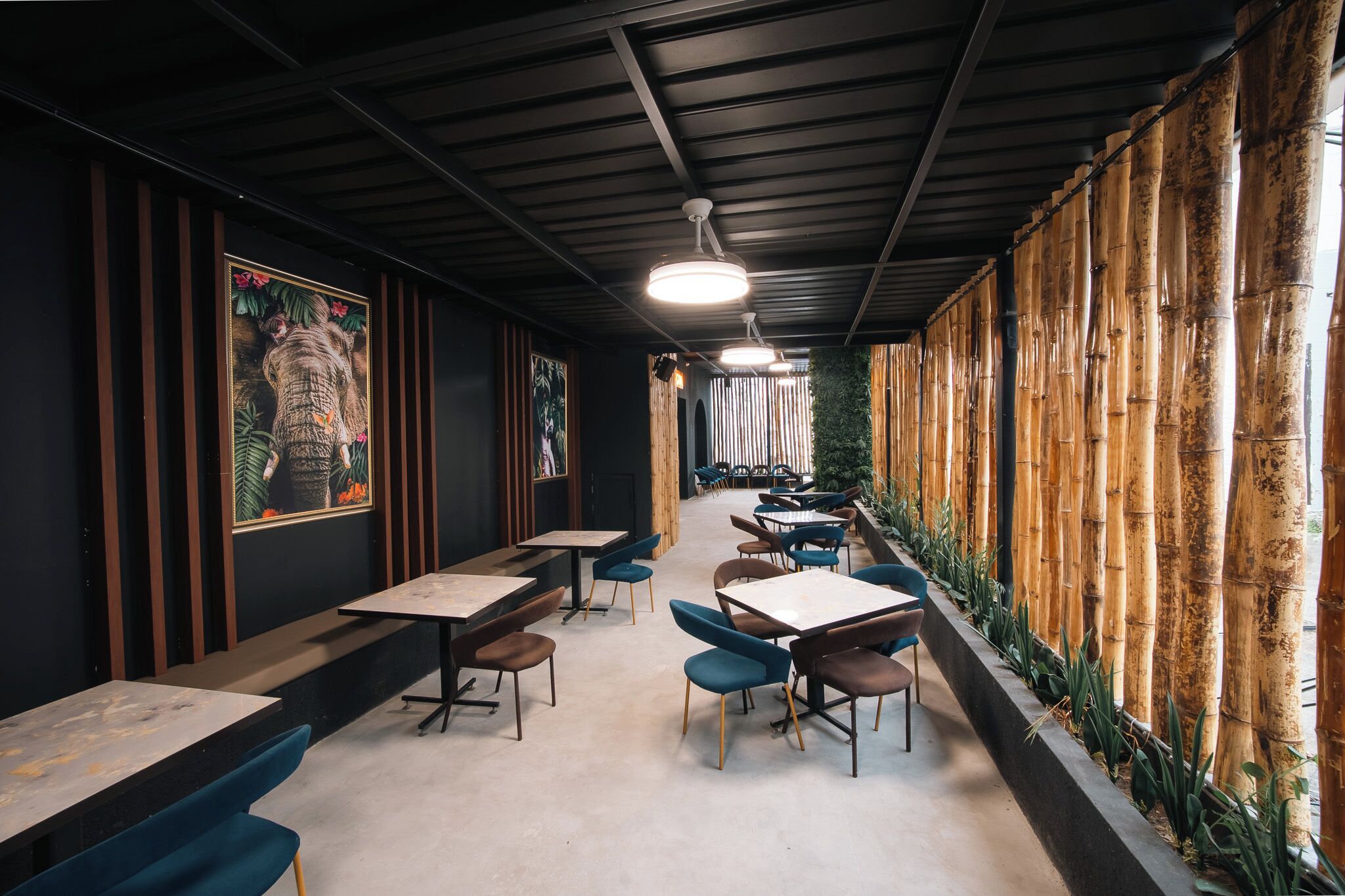 Un interior con mesas y sillas dispuestas para comer, un techo con vigas a la vista y una pared de bambú.