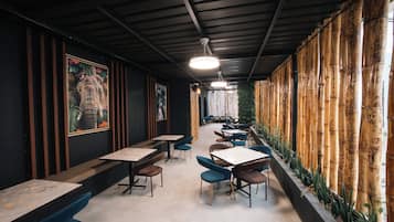 Un interior con mesas y sillas dispuestas para comer, un techo con vigas a la vista y una pared de bambú.