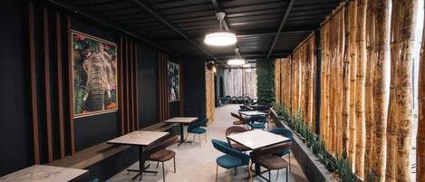 Un interior con mesas y sillas dispuestas para comer, un techo con vigas a la vista y una pared de bambú.
